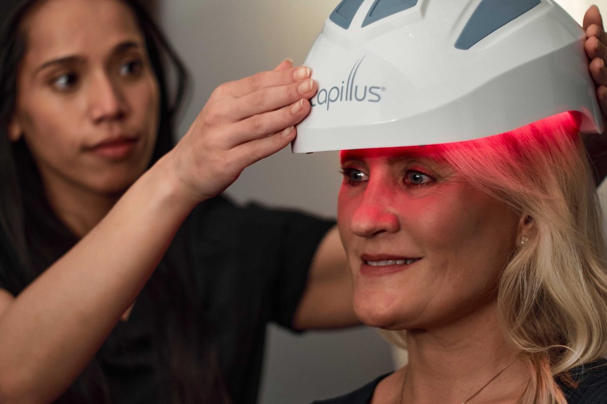 A staff member fitting a low-level laser therapy cap on a client at Hair Restoration Specialists of Atlanta